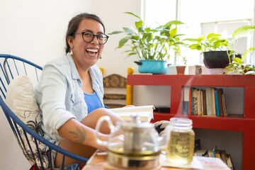 mexican tattooed millennial woman reading a book and laughing