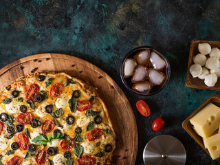 Pizza on a large wooden platter, ingredients, a knife and a glass of ice drink. Low angle view....