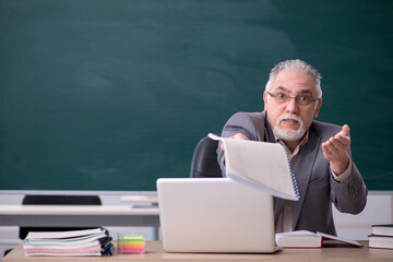 Old male teacher in front of blackboard