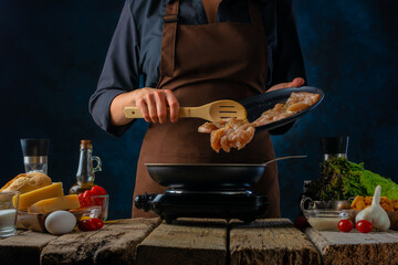 The cook fries chicken fillets in a pan for Caesar salad. Salad ingredients. Dark background....