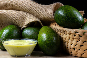 avocados fruits and avocado cream in glass bowl on the wooden table, with jute and black background in Brazil