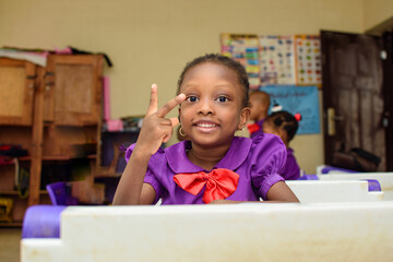 African girl child making happy gestures with fingers, wearing a purple school uniform while...