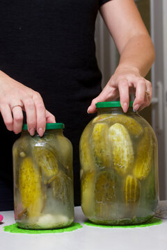 The woman closes the lid of a jar of cucumbers. Cucumbers are covered with pickling marinade. Harvest conservation.