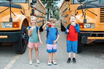Children boys and girl students friends eating apples healthy snack by yellow school bus outdoor....