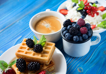 Waffles with blueberries, strawberry and blackberries with a cup of coffee.