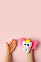 Little child holding felt tooth fairy toy in his hands on pink background. Easy and funny kids crafts, DIY, Happy Tooth Fairy greeting card, flyer, copy space, concept of tooth changes