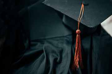 A black graduation cap with a brown tassel is placed on the graduation gown.