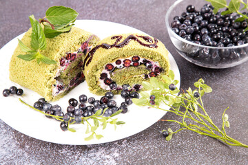 Sliced sponge roll with blueberries and matcha tea on a white plate. The concept of summer desserts