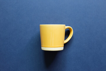 Yellow mug cup on blue background. top view, copy space