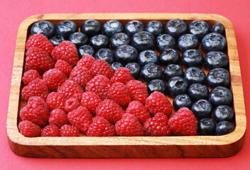 blueberries and raspberries on wooden plate, red background