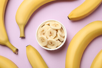 Bowl with cut bananas and whole fruits on pink background, flat lay