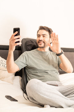 Man Working In Home Office From Bed With Cell Phone And Laptop And Back Massager