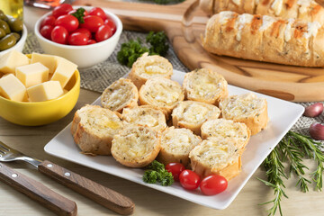 Garlic bread in white square plate on the table with cheese, rosemary, olives and cherry tomatoes.