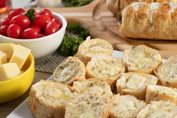Garlic bread in white square plate on the table with cheese, rosemary, olives and cherry tomatoes.