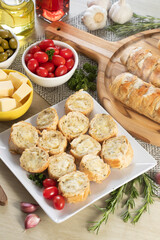 Garlic bread in white square plate on the table with cheese, rosemary, olives and cherry tomatoes.