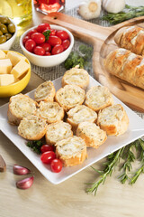 Garlic bread in white square plate on the table with cheese, rosemary, olives and cherry tomatoes. Top view.