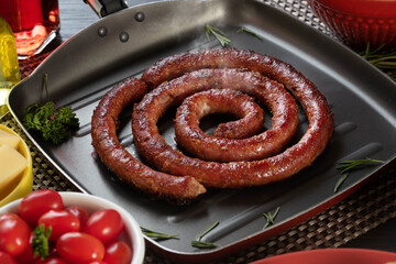 Sausage and garlic bread on a red plate on the barbecue table with appetizers, cheese, rosemary, olives and cherry tomatoes.
