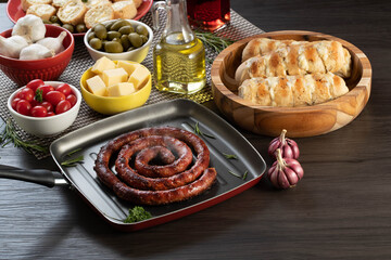 Sausage and garlic bread on a red plate on the barbecue table with appetizers, cheese, rosemary,...