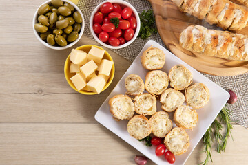 Garlic bread in white square plate on the table with cheese, rosemary, olives and cherry tomatoes. Top view.
