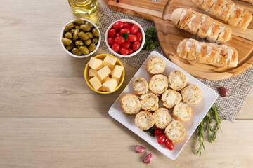 Garlic bread in white square plate on the table with cheese, rosemary, olives and cherry tomatoes. Top view.