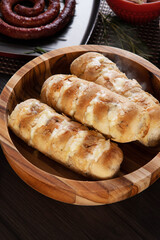 Garlic bread on a red plate on the barbecue table with sausage, cheese, rosemary, olives and cherry tomatoes.