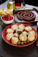Garlic bread on a red plate on the barbecue table with sausage, cheese, rosemary, olives and cherry tomatoes.