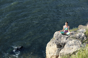Fototapeta na wymiar Young woman meditating on cliff near river. Space for text