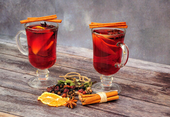 Two glasses of hot wine with citrus and a set of spices on a wooden table.