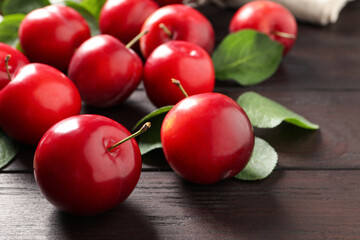 Delicious ripe cherry plums with leaves on wooden table, closeup