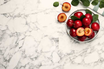 Delicious ripe cherry plums with leaves on white marble table, flat lay. Space for text