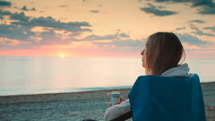 Fototapeta premium Close-up shot of Young woman drinking from thermos and sitting on camping chairs on the beach.
