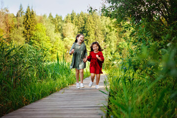 Two sisters run on a wooden deck in the city park in the open air. Freedom and carelessness. Happy childhood.