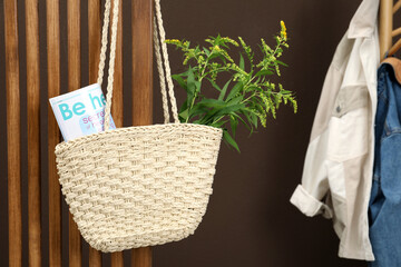 Stylish beach bag with plant and magazine hanging indoors. Space for text