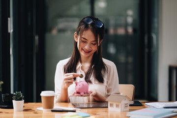 mortgage, investment, real estate and property concept - close up of woman putting money into pink piggy bank for loan or save for buy a new house