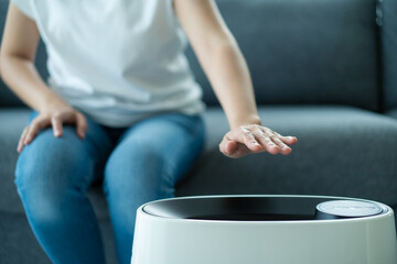 Asian woman turning on the modern air purifier while staying in the living room.