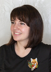 Portrait of a young woman with a handmade brooch on a light background. Facial expression, selective focus, beautiful people.