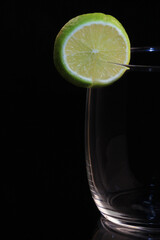 Close-up of glass vase with slice of lemon on black background.  Drink concept and texture