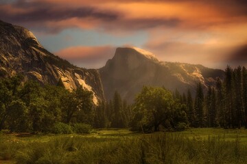 This image captures the beauty of Yosemite's half dome landscape with a moody sunset illuminating the rock formations and trees.