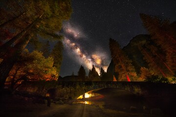 This image features the a magical view of Yosemite, over a tree lined bridge with a night sky...