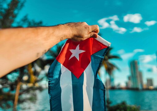 person holding a flag cuba cuban freedom miami usa sky blue palms buildings sea 