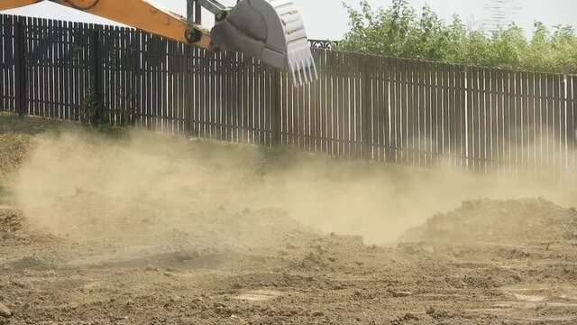 construction excavator excavation - dusty soil is poured from a large steel bucket to the ground. Hot summer sunny day