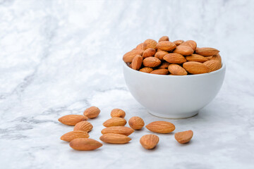 Almonds nuts in white bowl on marble background.	