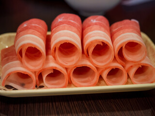 closeup rolls fresh raw pork slices on the dish, ingredient for hot pot