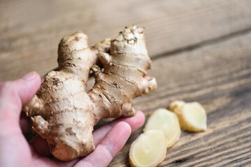 Fresh ginger root on hand with sliced ginger on wooden background