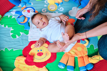 Baby lying on colorful play mat while playing with his mother.