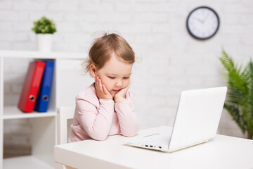 cute thoughtful little girl using laptop at home or in class room