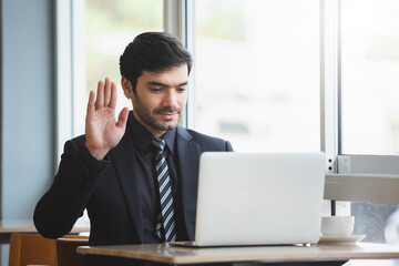 Obraz premium businessman raising hand to greet making video call on laptop. conference online. working new normal. Man working on computer laptop.