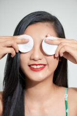 Pretty beauty young Asian woman covering her eyes with cotton pad over white isolated background. Healthy skin and cosmetics concept.