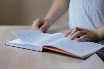 The boy is reading a book. Hand on the book. Book on the table. The boy reads a book on the table. A child reads a bookExpanded book.