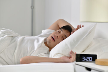  Young Asian man sleeping and snoring loudly lying in the bed.